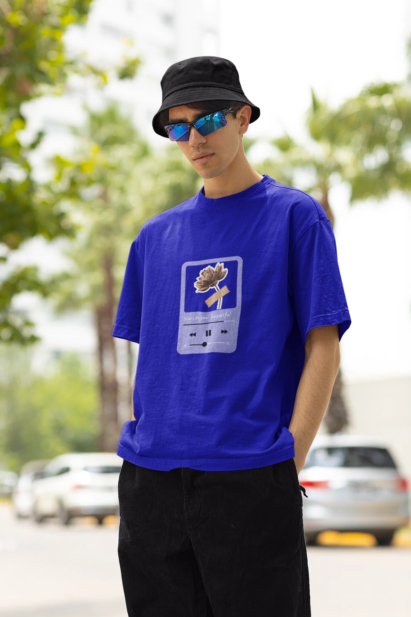 Left side view of a male model wearing a royal blue oversized t-shirt featuring a design inspired by Alessia Cara's song "Scars to Your Beautiful." The design includes flowers and a message of self-love. Ideal for fans of Alessia Cara and those who appreciate messages of empowerment.