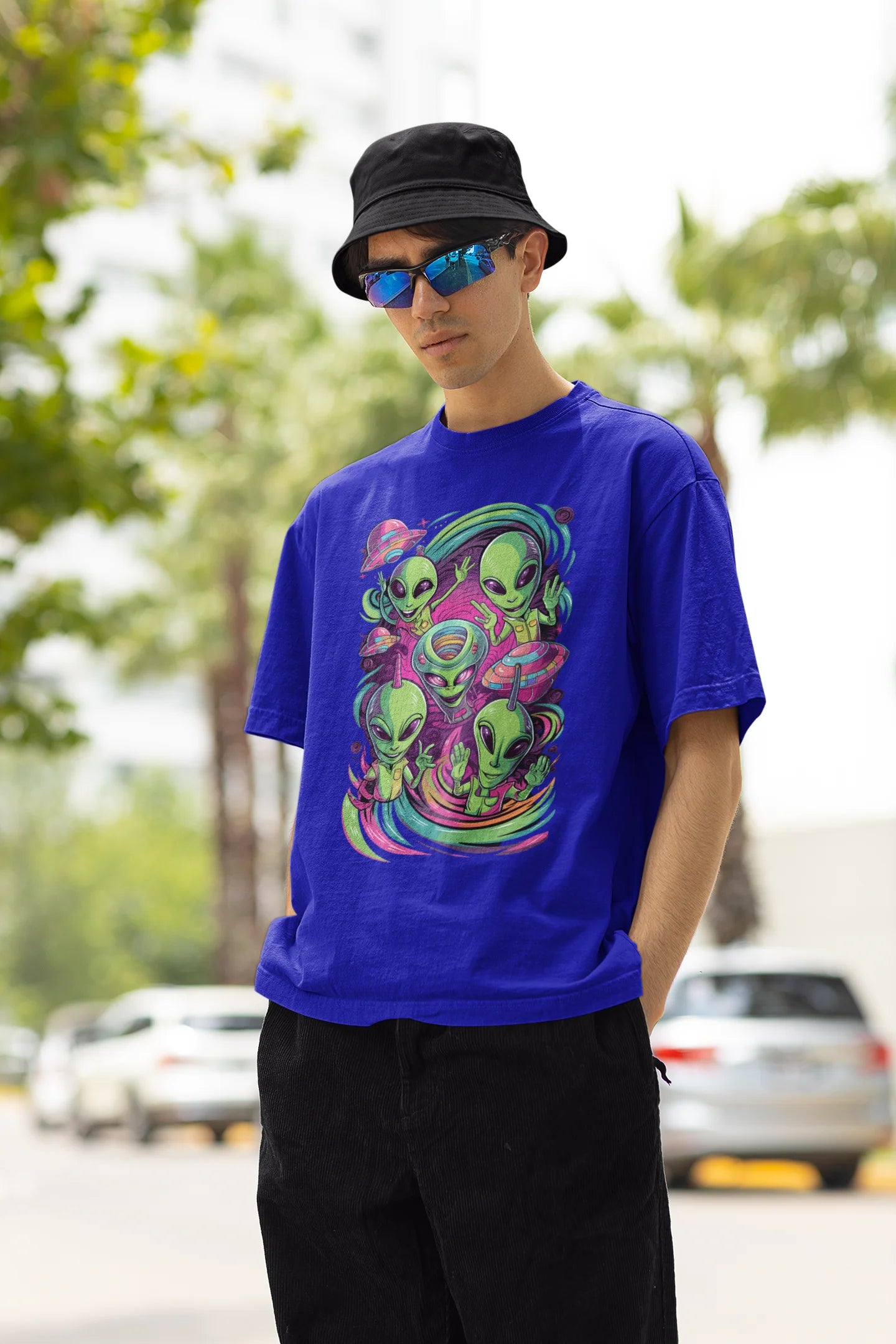 Left side view of a male model wearing a royal blue oversized t-shirt with a psychedelic design featuring green aliens and spaceships, perfect for a hippie, trance, or groovy style.