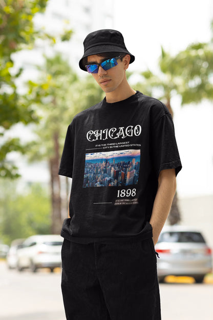 Right side view of male model wearing a black oversized t-shirt with a Chicago skyline design, offering a relaxed urban aesthetic.
