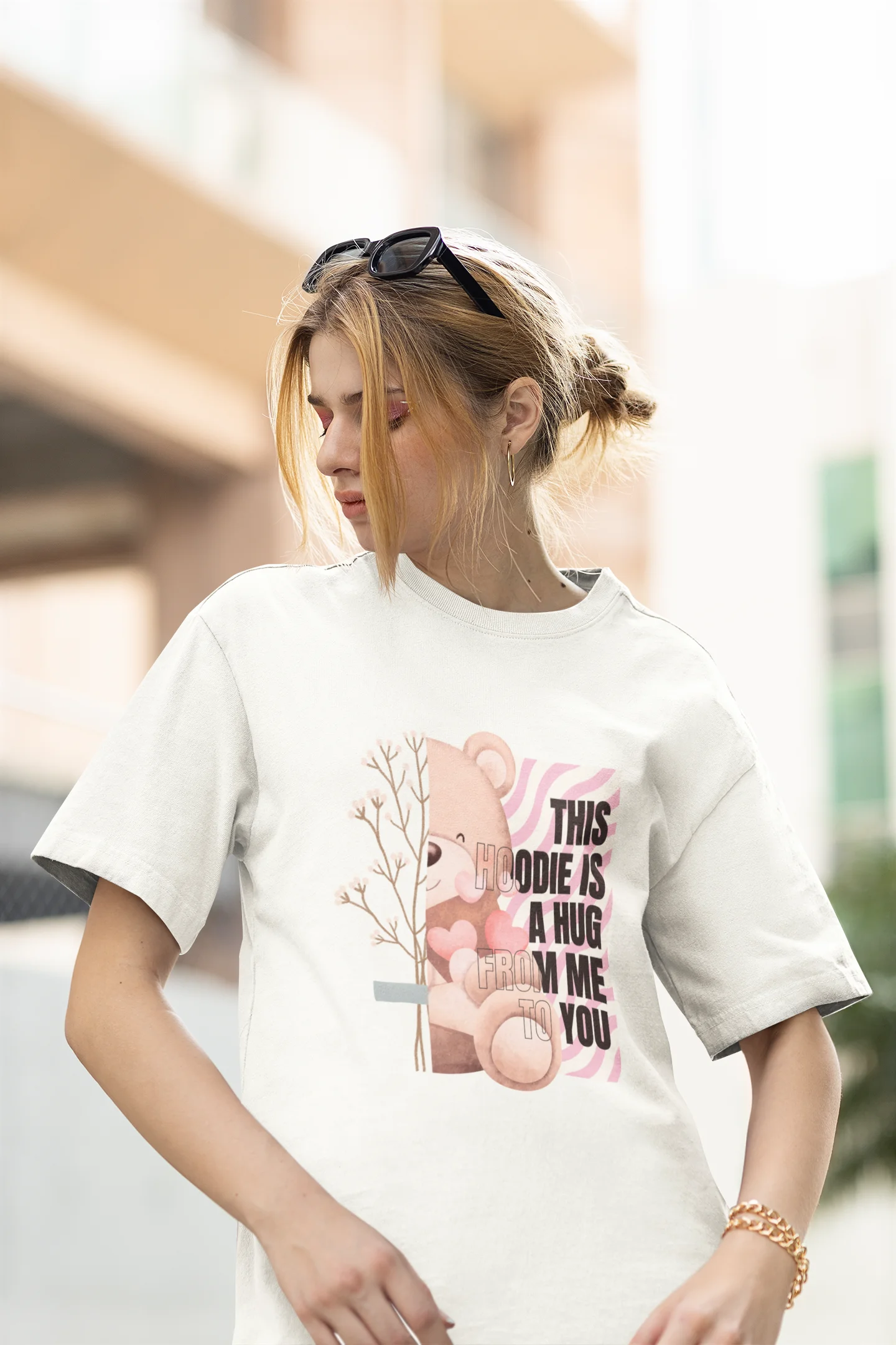 First front view of a female model wearing an off-white oversized t-shirt with a heartwarming design of a teddy bear offering a hug, offering a comforting and relaxing aesthetic.