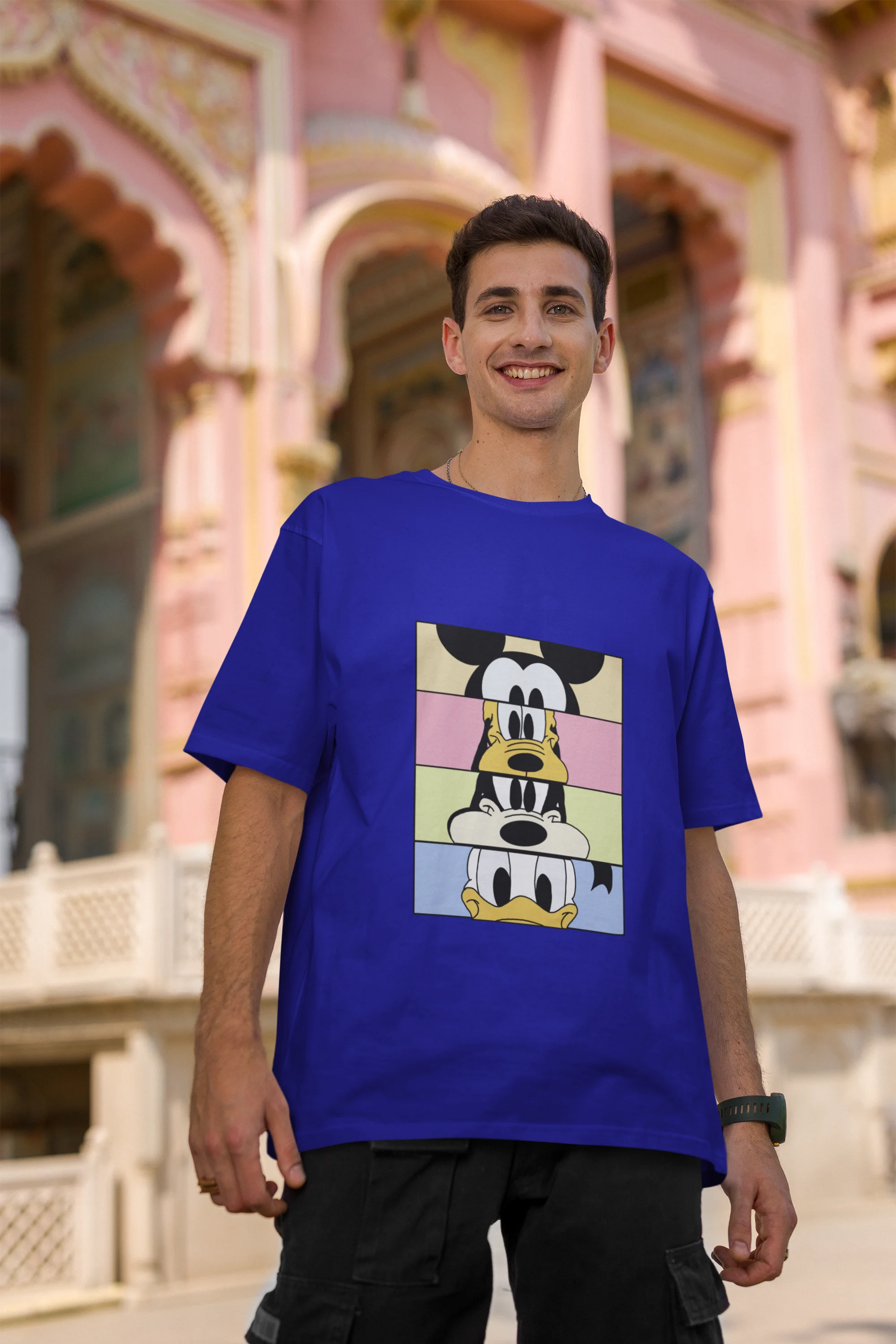 Second image of male Model showcasing blue oversized t-shirt inspired by Mickey Mouse Clubhouse characters: Mickey Mouse, Donald Duck, Goofy, and Minnie Mouse