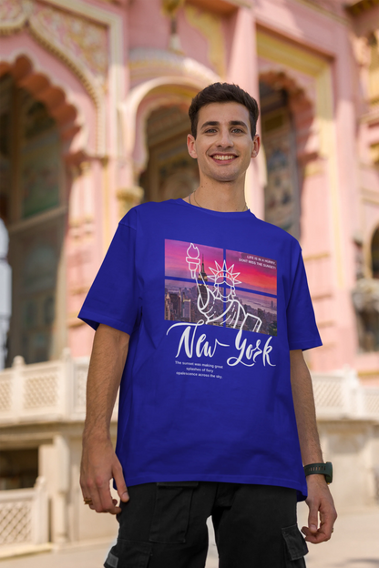 Second front view of a male model wearing a royal blue oversized t-shirt with a New York City skyline design, offering a relaxed urban aesthetic.