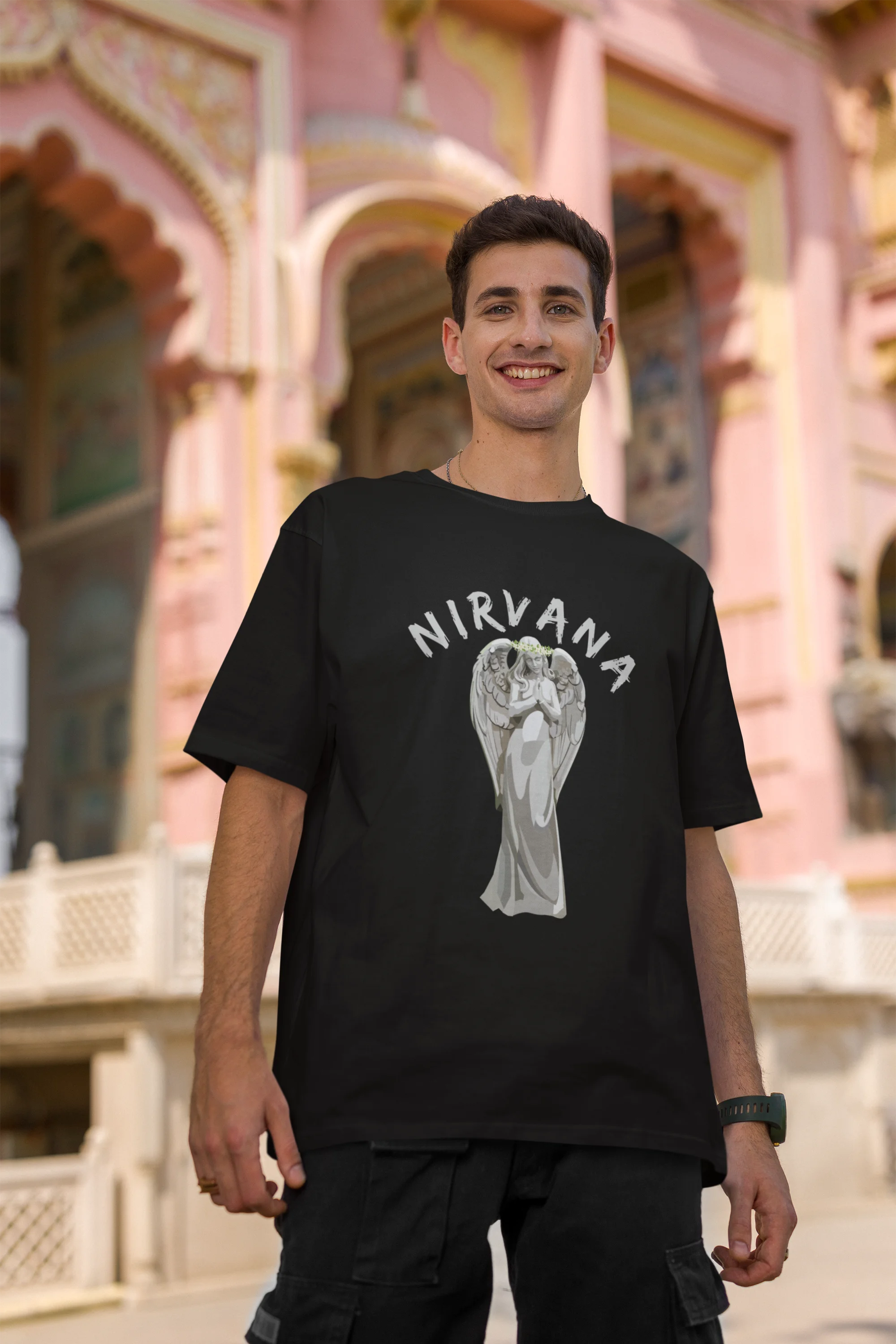 First front image of male model wearing a black oversized t-shirt featuring a design of a winged angel with the text "Nirvana" above it. Ideal for fans of Nirvana and those who love grunge aesthetics.